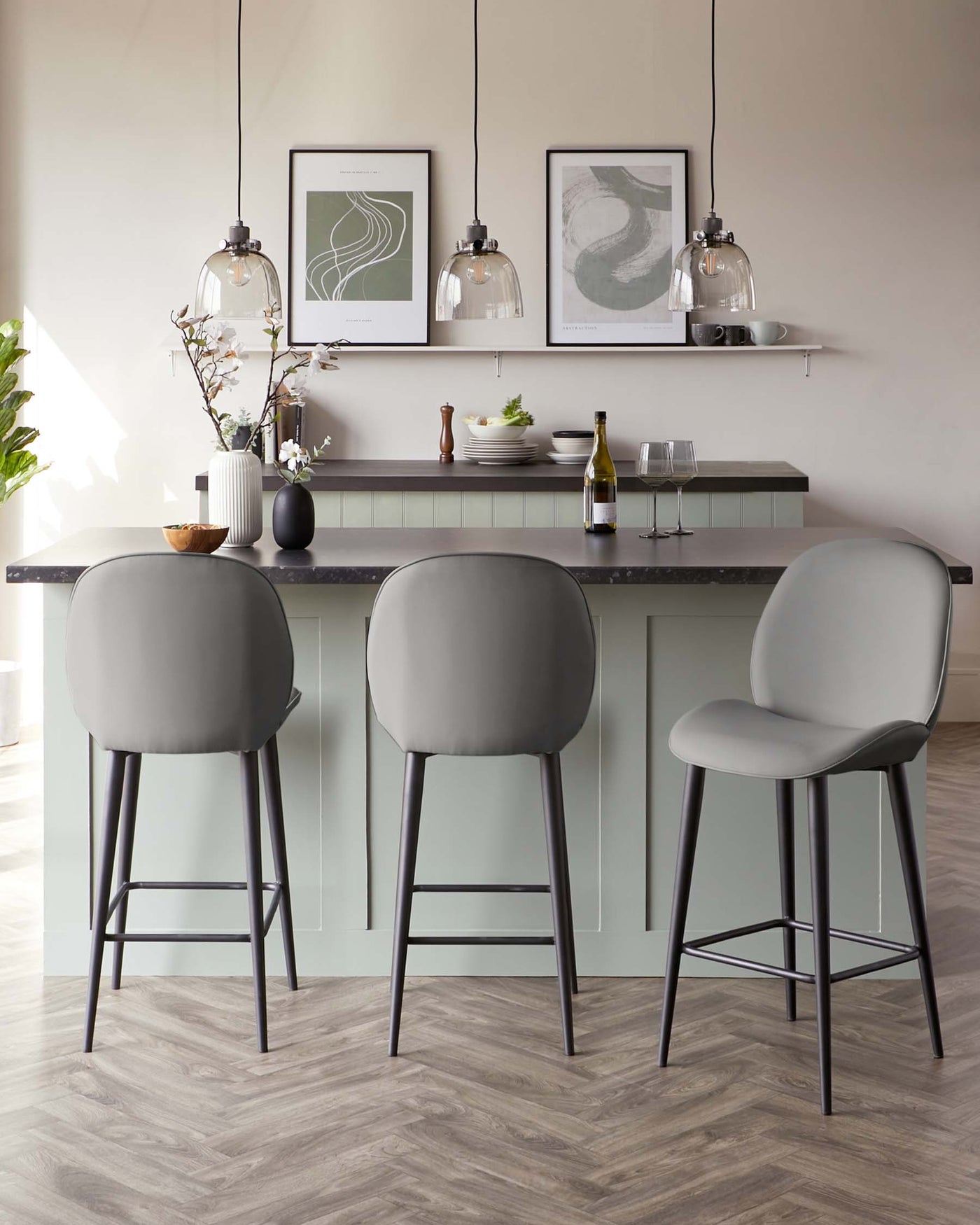 Modern kitchen island with elegant grey counter and sage green cabinetry, complemented by sleek bar stools with curved backrests and slender black metal legs.