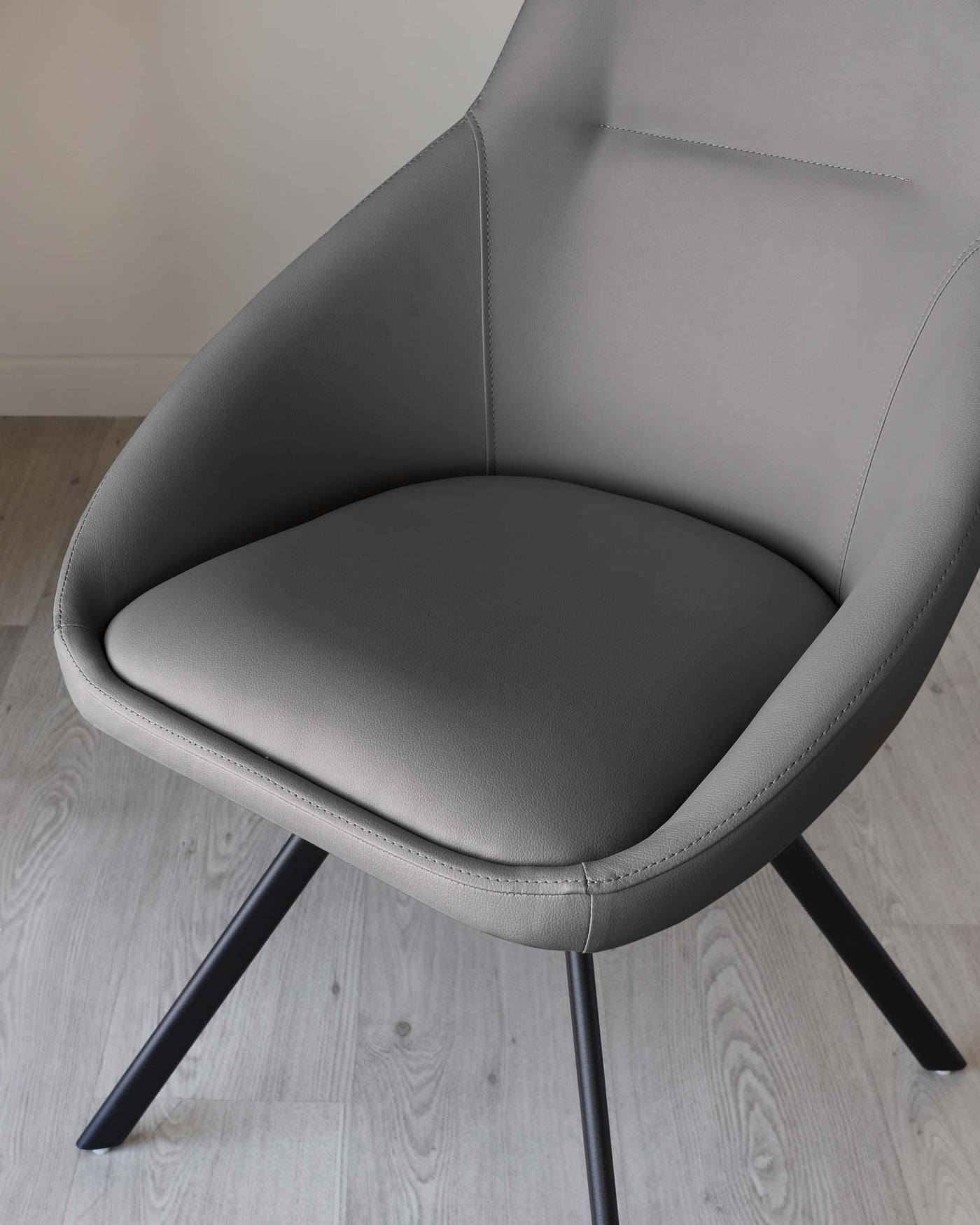 Modern grey upholstered accent chair with a curved backrest and a cushioned seat on black metal legs against a light wooden floor background.