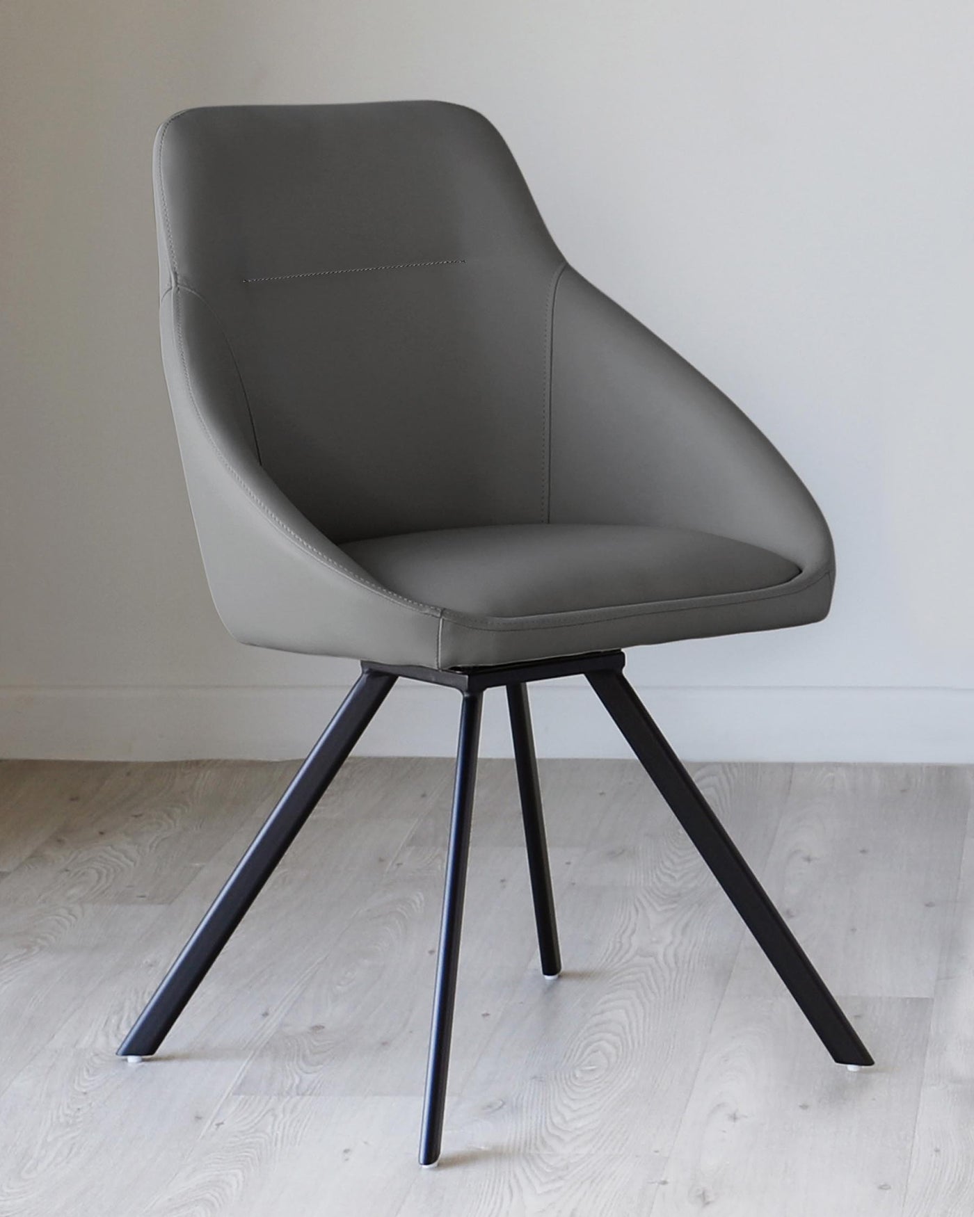 Modern grey upholstered dining chair with a curved backrest and minimalist stitch detailing, set on a sleek black four-legged metal base.