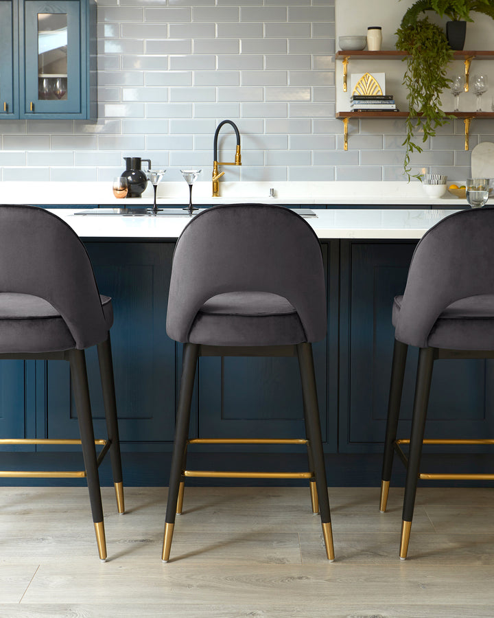 Elegant modern bar stools with dark grey upholstered seats and backs, featuring sleek black frames with gold accents including footrests and leg tips, set against a kitchen island.