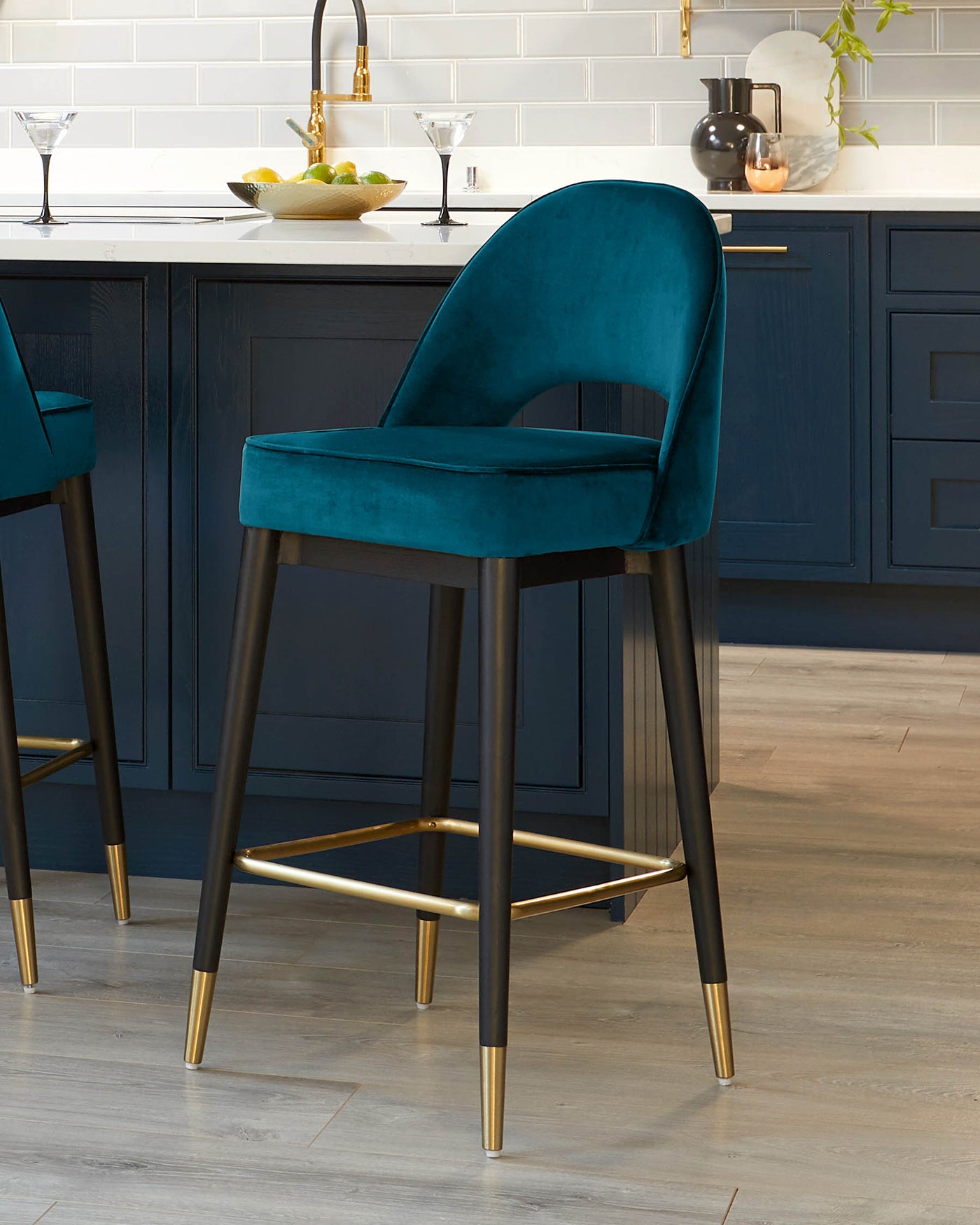 Elegant modern bar stool with plush teal velvet upholstery and a curved backrest, supported by a sleek black metal frame with gold accents on the legs and footrest.