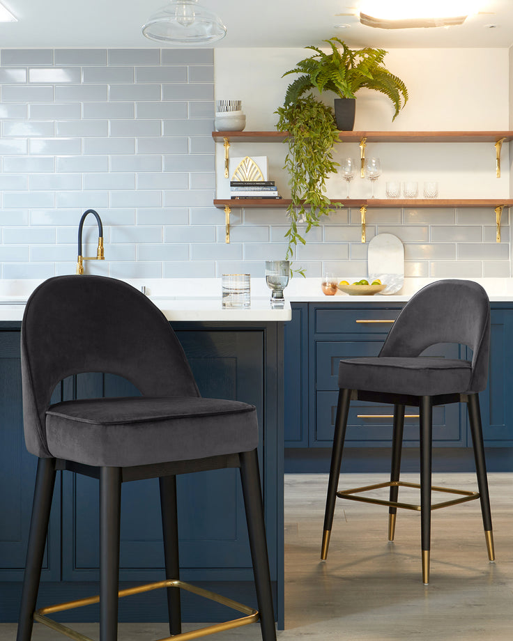 Two elegant velvet upholstered bar stools with curved backrests and black wooden legs accented with gold footrests.