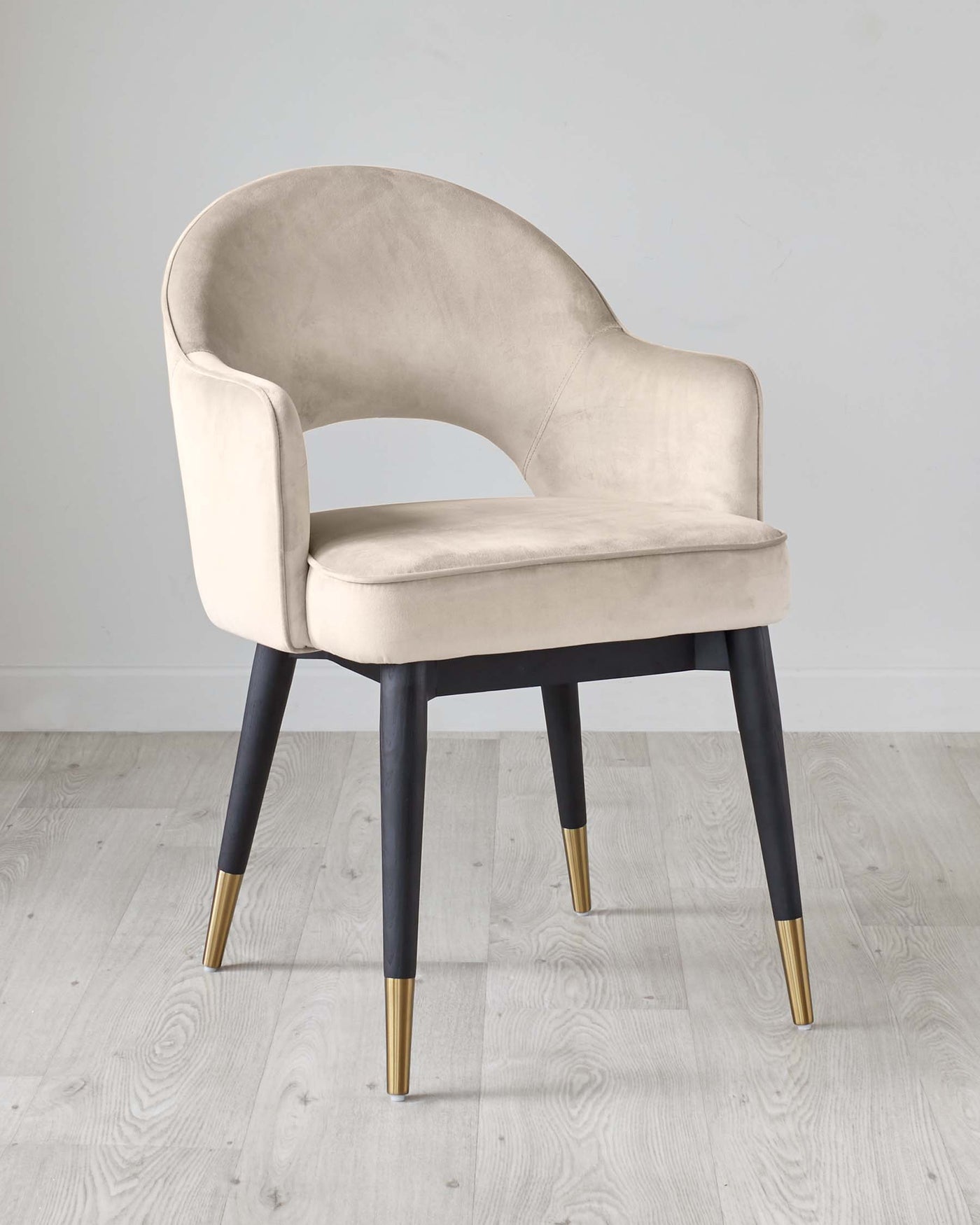 Elegant modern accent chair with a curved backrest and plush light beige velvet upholstery. It features dark wooden tapered legs with stylish gold-coloured tips, creating a chic contrast. Perfect for adding a luxurious touch to any room decor.