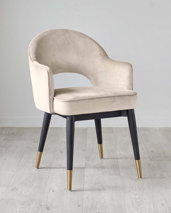 Elegant modern accent chair with a curved backrest and plush light beige velvet upholstery. It features dark wooden tapered legs with stylish gold-coloured tips, creating a chic contrast. Perfect for adding a luxurious touch to any room decor.