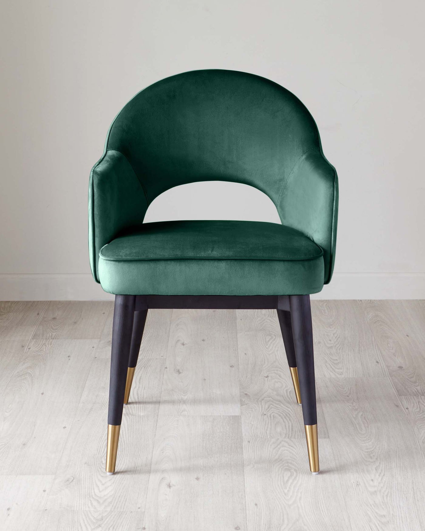 Elegant dark green velvet accent chair with a rounded backrest, plush seating, and tapered dark wooden legs with gold metal tips on a light wooden floor.