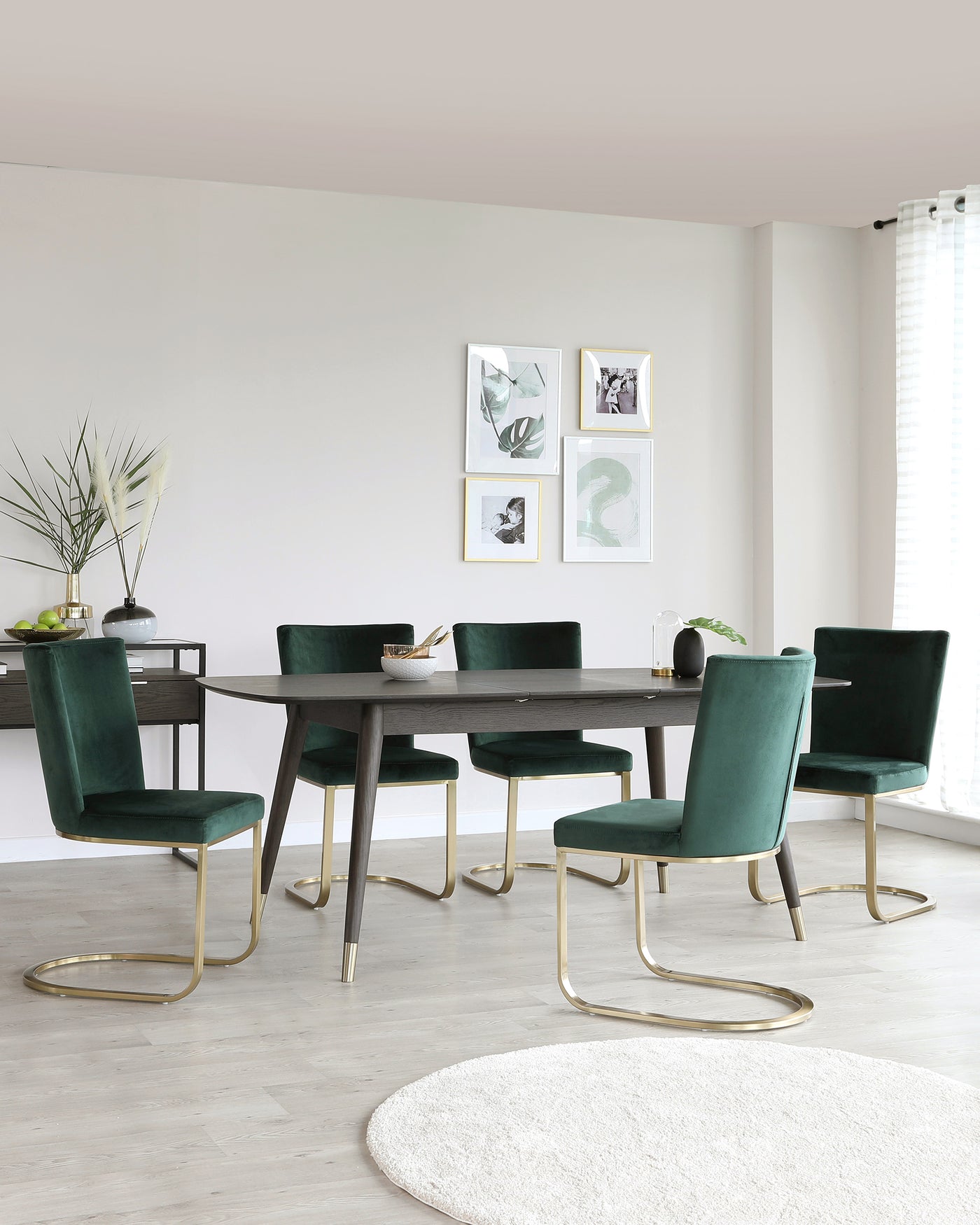 Elegant dining room setup featuring a modern dark wood dining table with sleek, straight lines and a set of six luxurious velvet upholstered chairs in a rich emerald green. The chairs have brass-finished metal cantilever bases that provide a stylish contrast to the wood, infusing a sophisticated touch to the contemporary design. A matching dark wood side table adorned with decorative vases complements the ensemble.