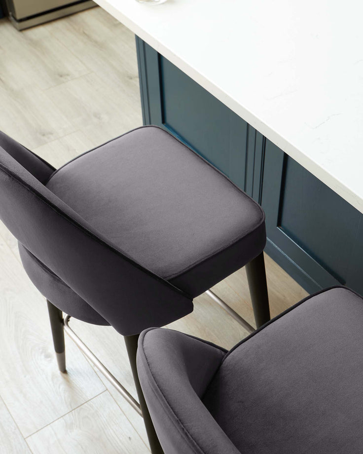 A modern charcoal-grey upholstered dining chair with a sleek silhouette and slender black metal legs positioned beside a white countertop with a teal blue base. The chair features a comfortable padded seat and backrest.