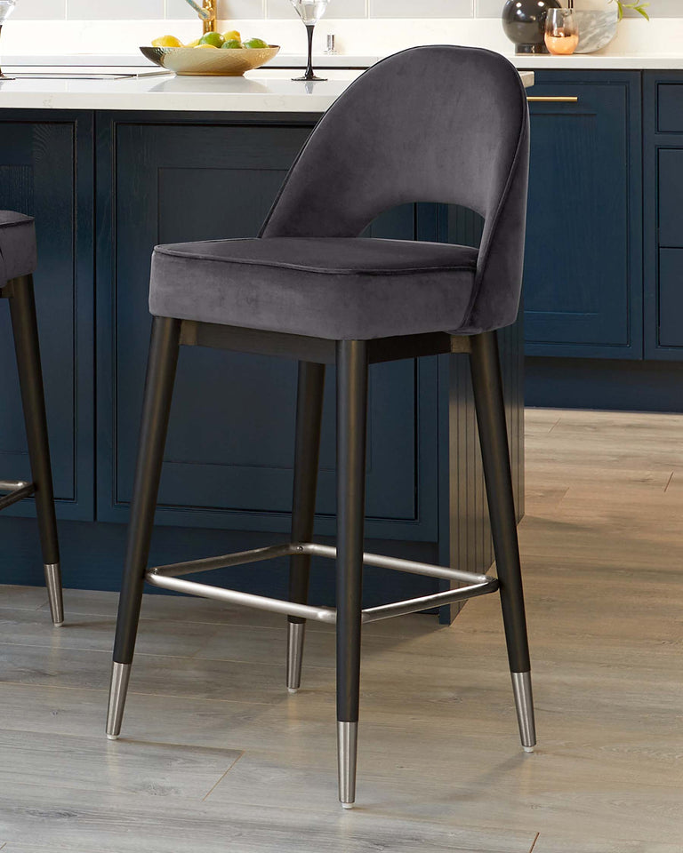 Elegant modern bar stool with plush, curved backrest and seat upholstered in dark grey velvet fabric, featuring sleek black metal legs with a contrasting stainless steel footrest.