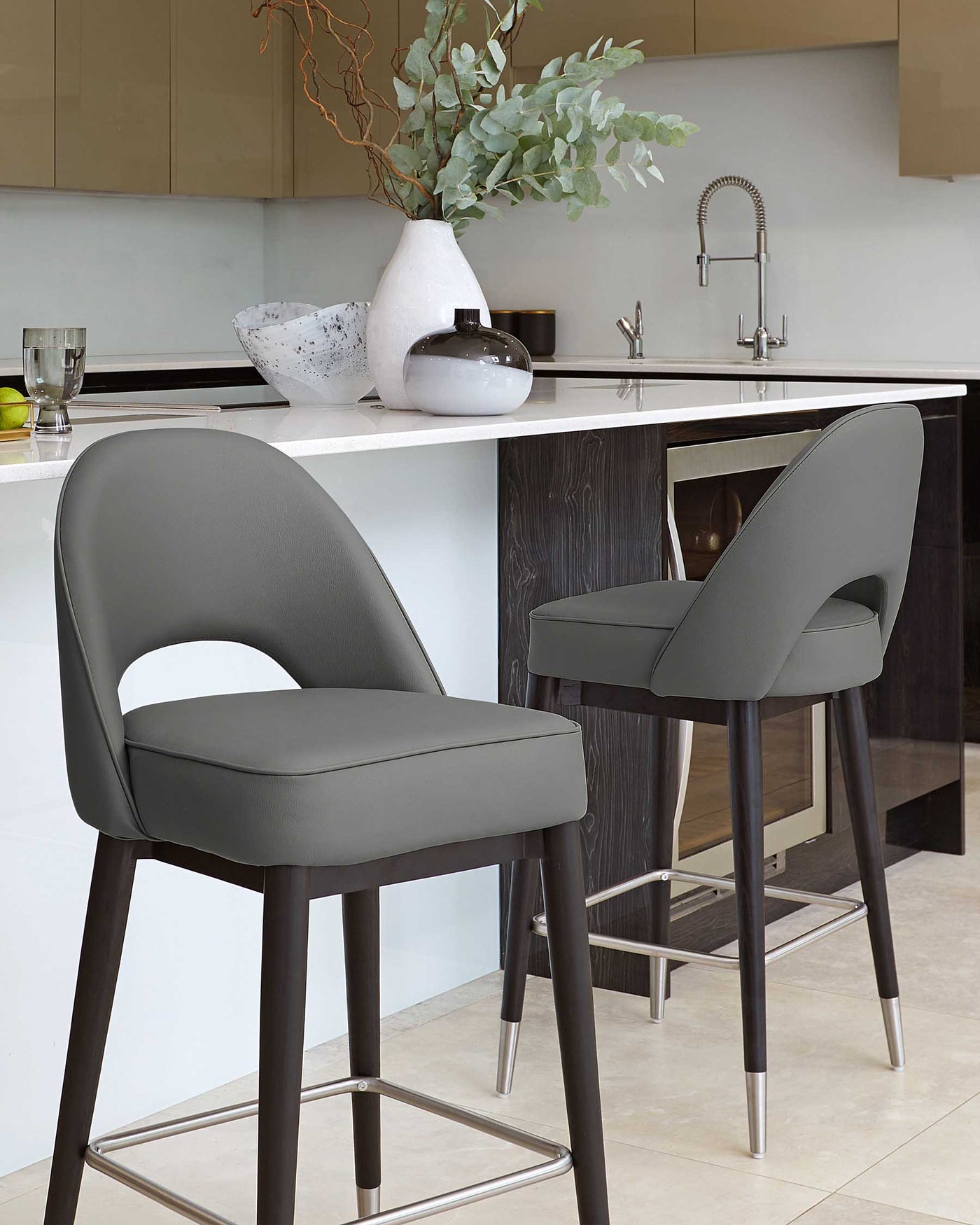 Two modern bar stools with dark grey upholstery and dark wooden legs, featuring a low back design and a metallic footrest.