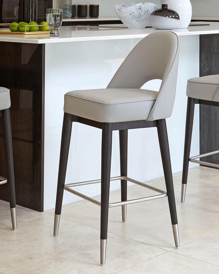 Modern bar stool with a grey upholstered seat and a high backrest, featuring dark wooden legs with metallic footrests and tips, positioned against a kitchen island with a white countertop.