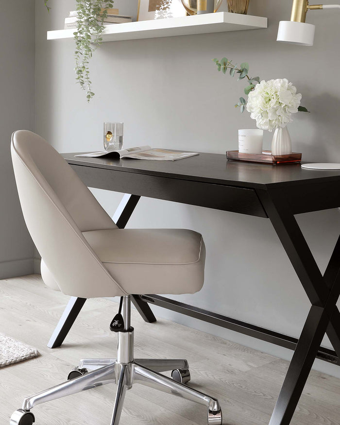 Contemporary home office setting featuring a black wooden desk with distinctive X-shaped legs and a sleek desktop, paired with a cream upholstered swivel chair with a curved backrest, cushioned seat, and chrome five-spoke base with casters.