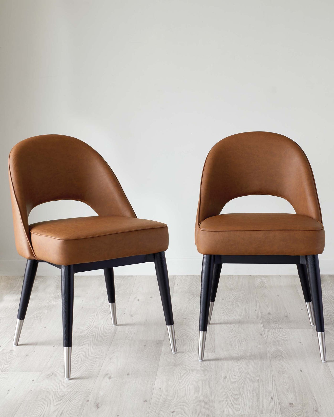 Two modern dining chairs with brown leather upholstery and contrasting dark wooden legs with metallic silver tips.