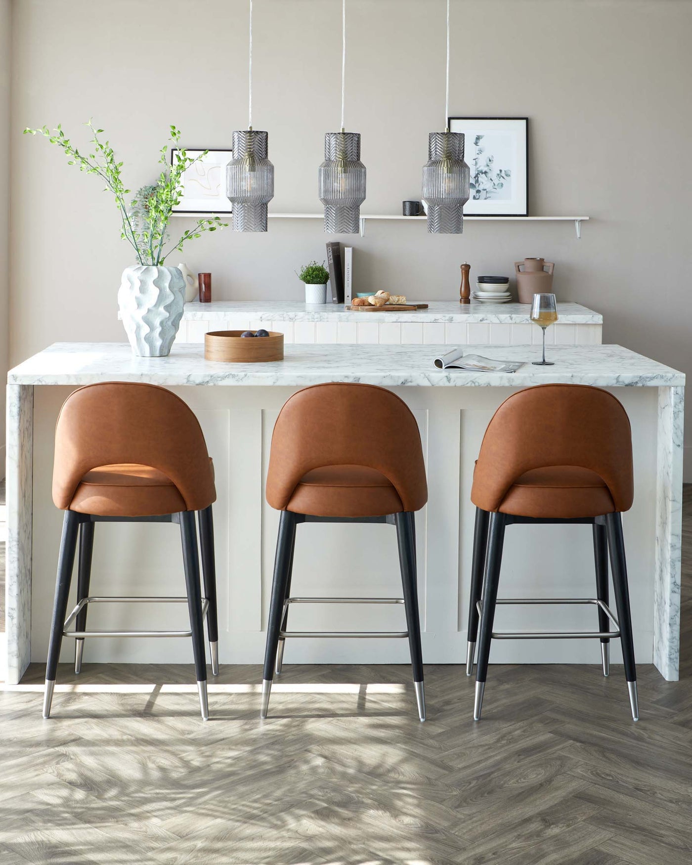 Three modern bar stools with brown leather seats and black metal legs in front of a white marble countertop.