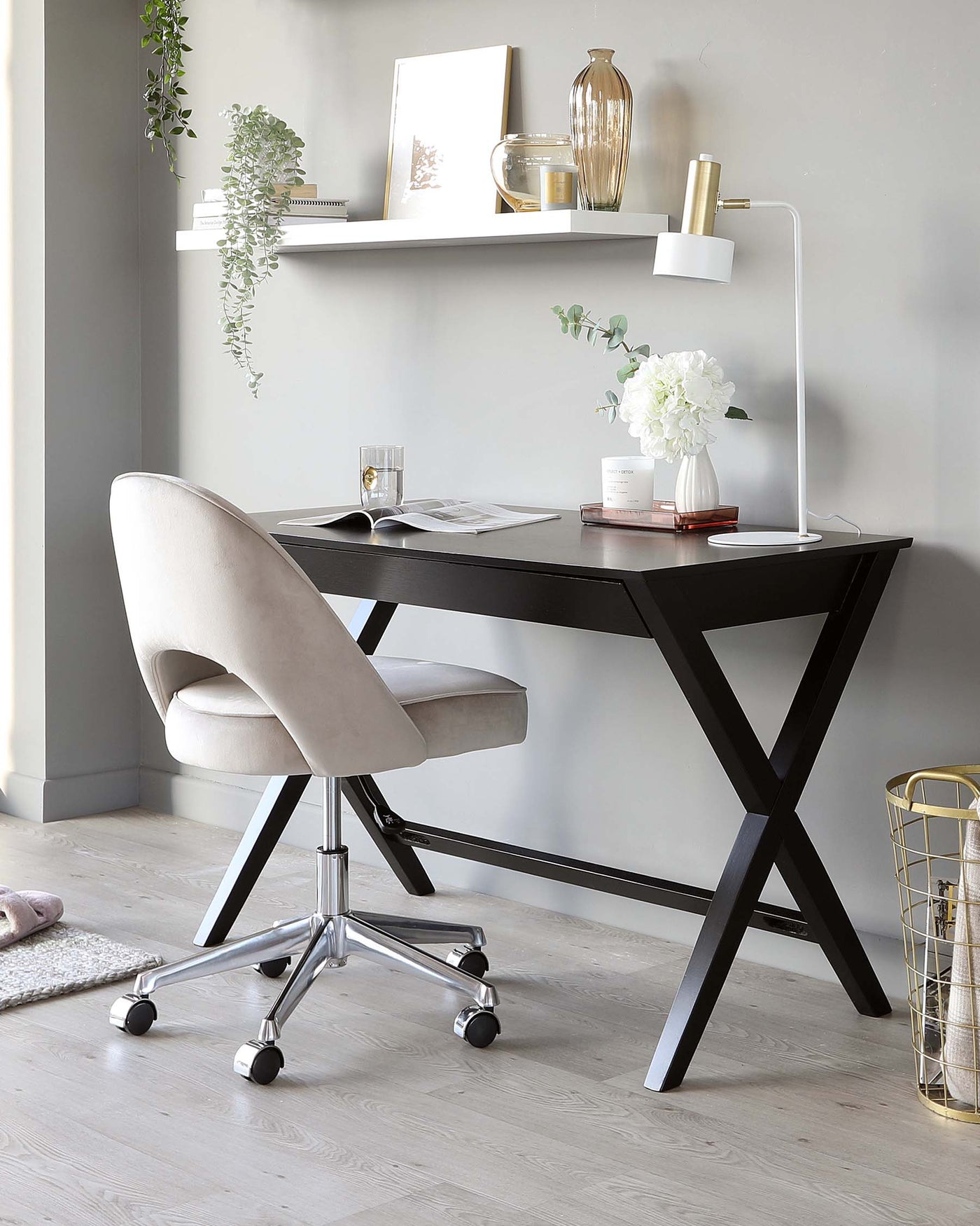 A modern workspace featuring a matte black writing desk with X-shaped legs and a sleek tabletop, paired with a beige upholstered office chair on a chrome swivel base with caster wheels.