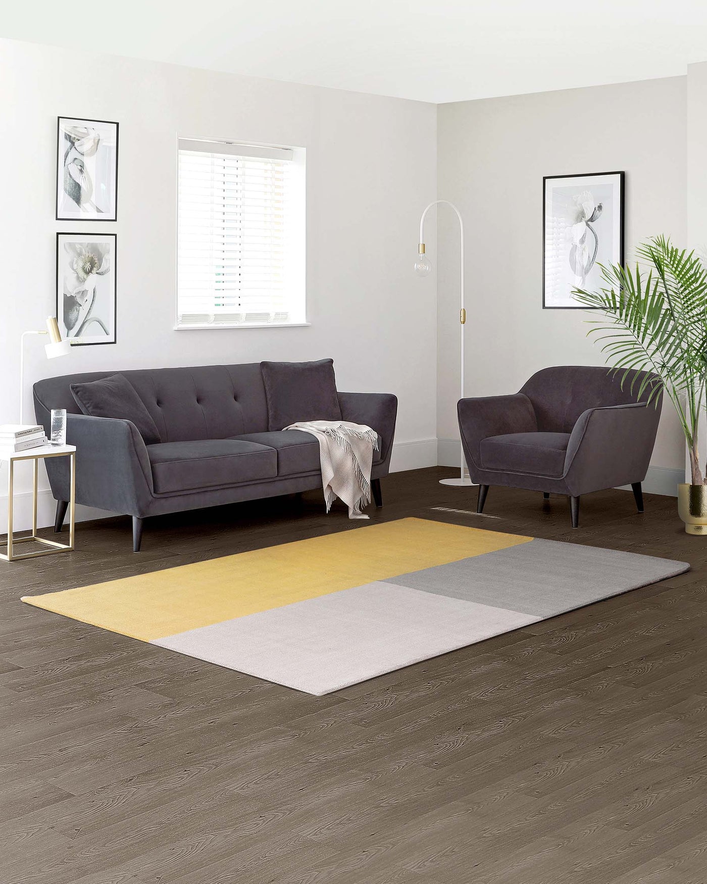 Contemporary living room furniture set featuring a three-seater sofa and a matching armchair upholstered in grey fabric with tufting on the back cushions. A white and gold minimalist side table sits beside the sofa.