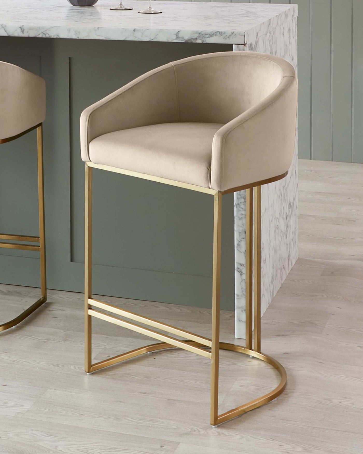 Elegant modern bar stool with a beige upholstered seat and curved backrest, set on sleek gold-finished metal legs.