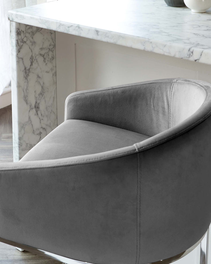 Elegant modern furniture featuring a luxurious marble-topped console table with bold veining and a plush velvet-upholstered curved armchair in a soft grey tone.