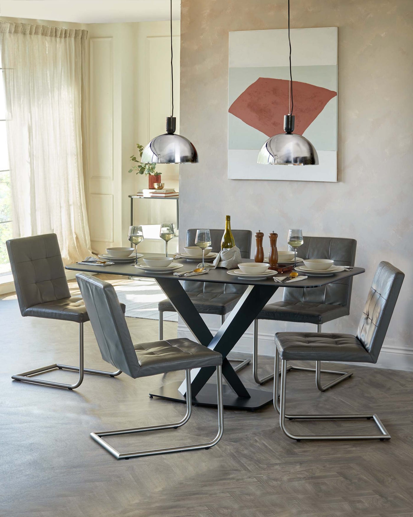 Modern dining room featuring a round glass-top table with a bold, black X-shaped base and four contemporary leather-upholstered chairs with sleek chrome cantilever frames.