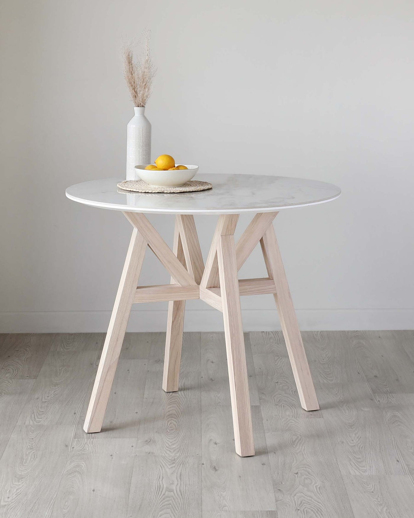 Round marble-top table with a unique wooden base consisting of interlocking timber legs in a light natural finish, displayed on a grey laminate floor against a plain light grey wall.
