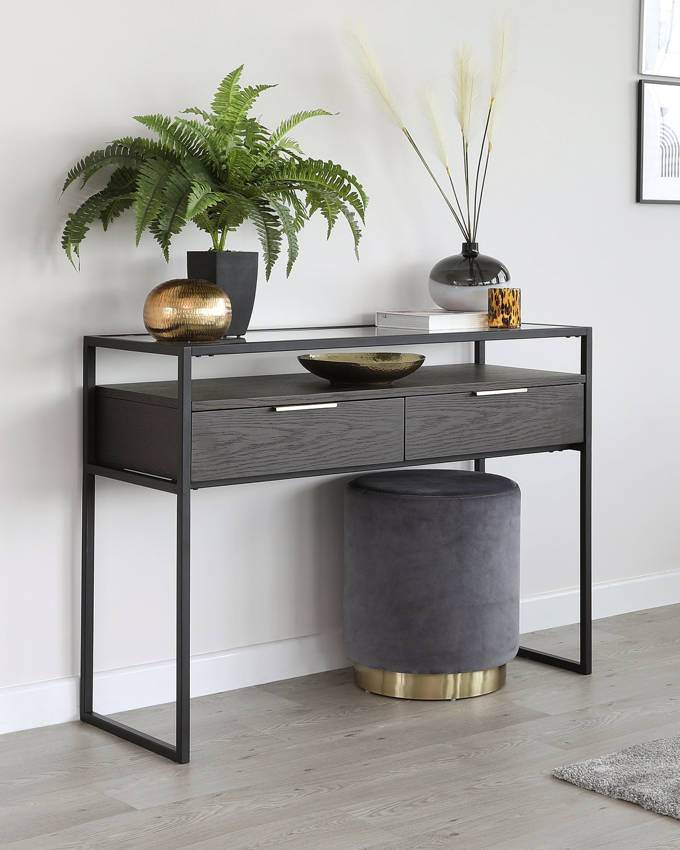 Modern minimalist console table with a sleek black metal frame and two grey wood-textured drawers, paired with a round, velvet-upholstered ottoman in a deep grey tone featuring a golden base.
