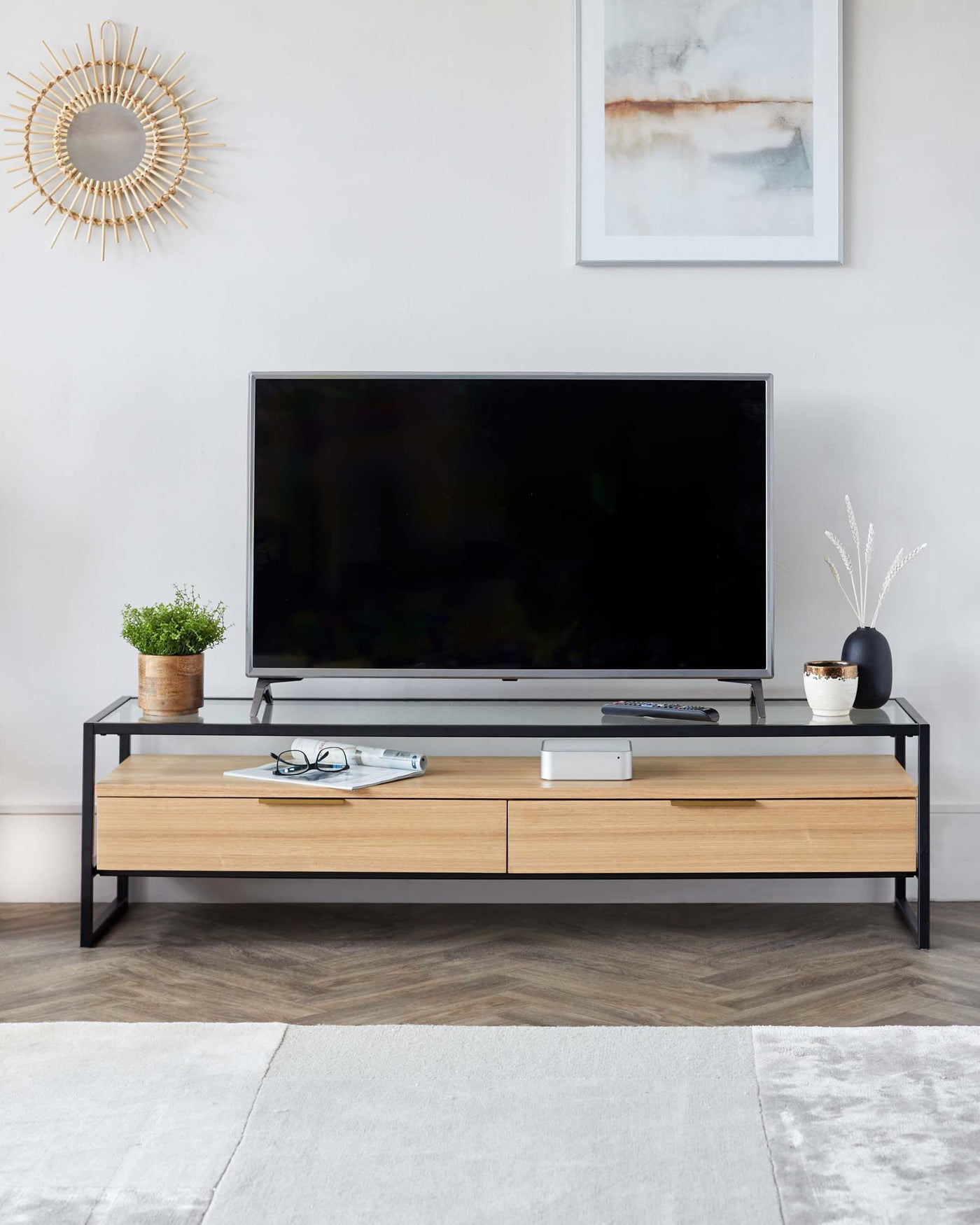 Modern minimalist TV stand in light oak finish with two drawers and one open shelf, featuring a black metal frame, situated on a light wood floor with a partial grey area rug below.