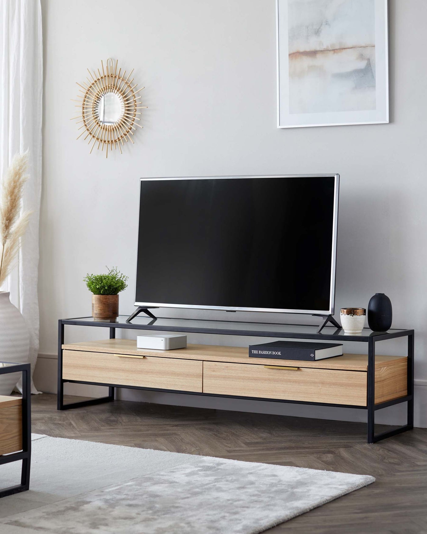 Modern minimalist TV stand with a sleek black metal frame and light wood drawers, featuring a spacious tabletop for electronic devices.
