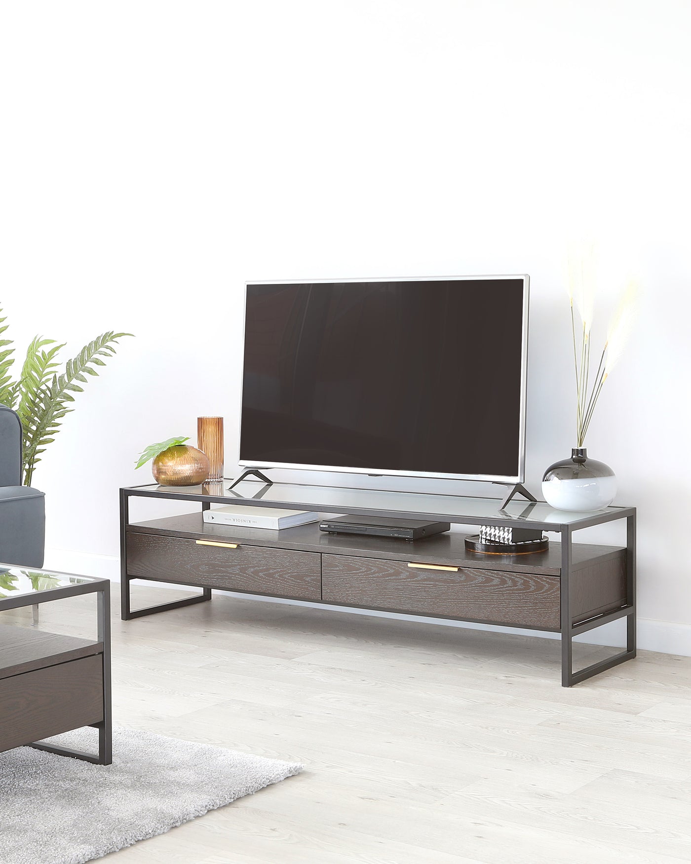 Modern minimalist TV stand with a dark wood finish and metal frame, featuring two drawers and an open shelf, accompanied by a sleek matching coffee table with a glass top and a wooden drawer.