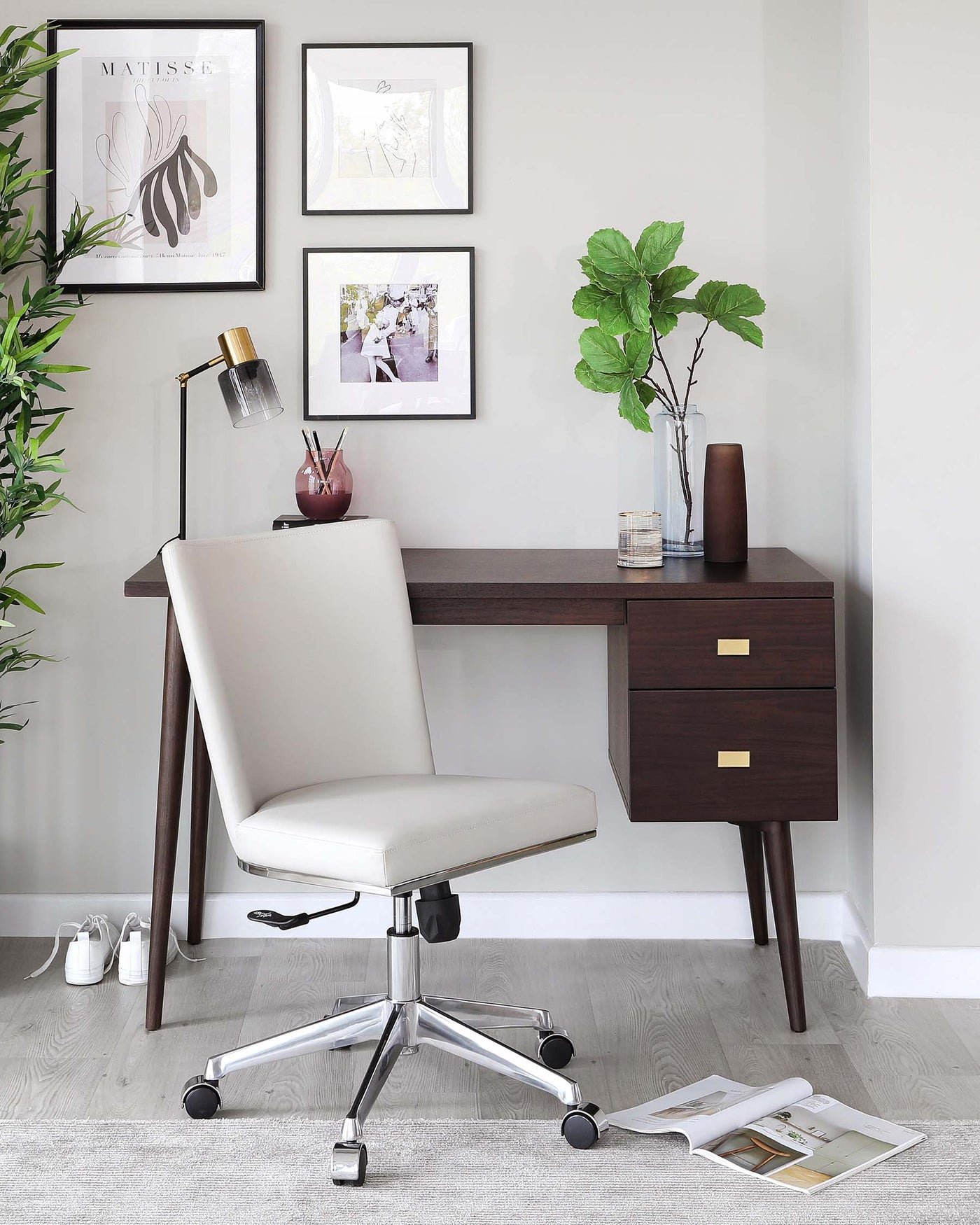 Modern home office setup featuring a sleek, walnut-finish writing desk with clean lines, two drawers with brass handles, and angled legs, paired with a cream-colored, upholstered office chair with a high backrest, armless design, and five-point chrome base with casters.