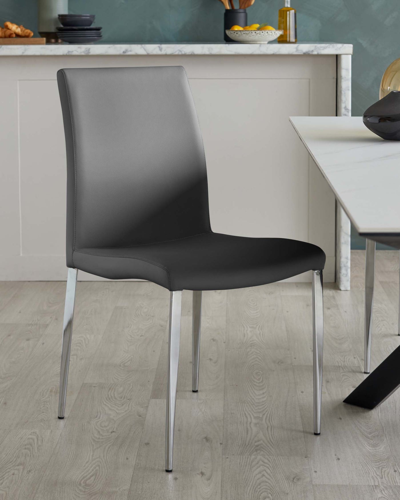 Modern dining chair with a sleek, dark grey faux leather upholstery and four polished chrome legs. The chair has a minimalist design with a slightly curved backrest and a padded seat for comfort.