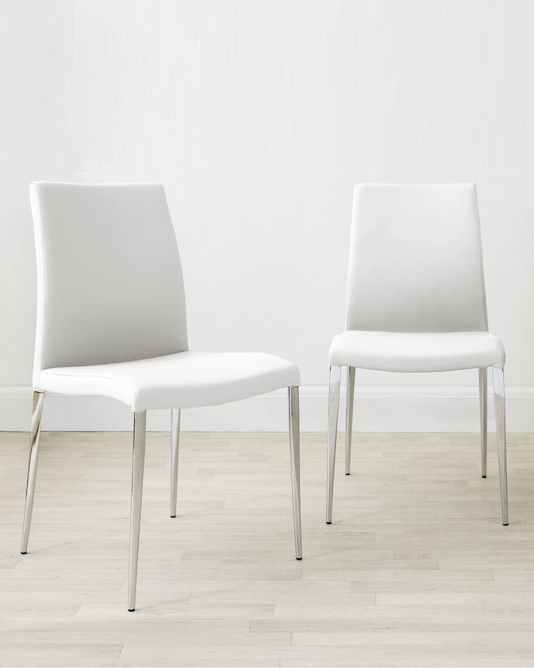 Two modern white upholstered dining chairs with sleek silver metal legs, positioned on a light wood floor against a white wall.