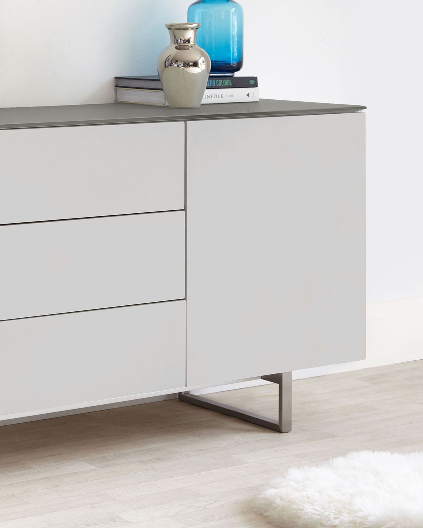 Modern minimalist light grey sideboard with sleek lines, featuring three flush drawers and a distinctive metal base in a brushed finish.