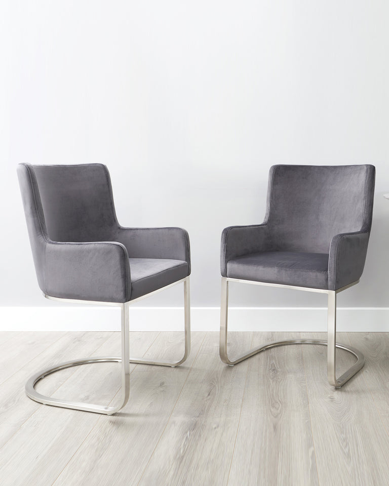 Two modern grey velvet accent chairs with sleek, chrome-finished metal cantilever bases featured on a light wooden floor against a white background.