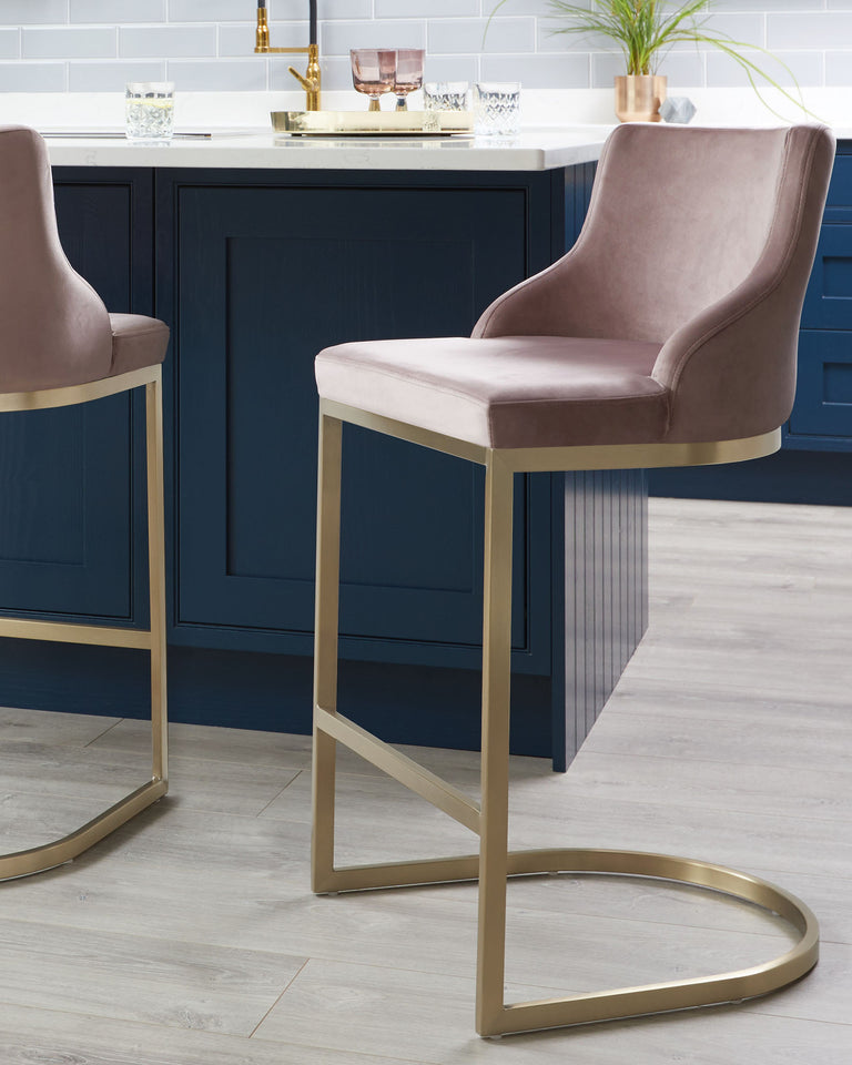 Luxurious velvet-upholstered bar stools with high backs and polished gold metal frame bases, in a contemporary kitchen setting with a navy blue island and brass accents.