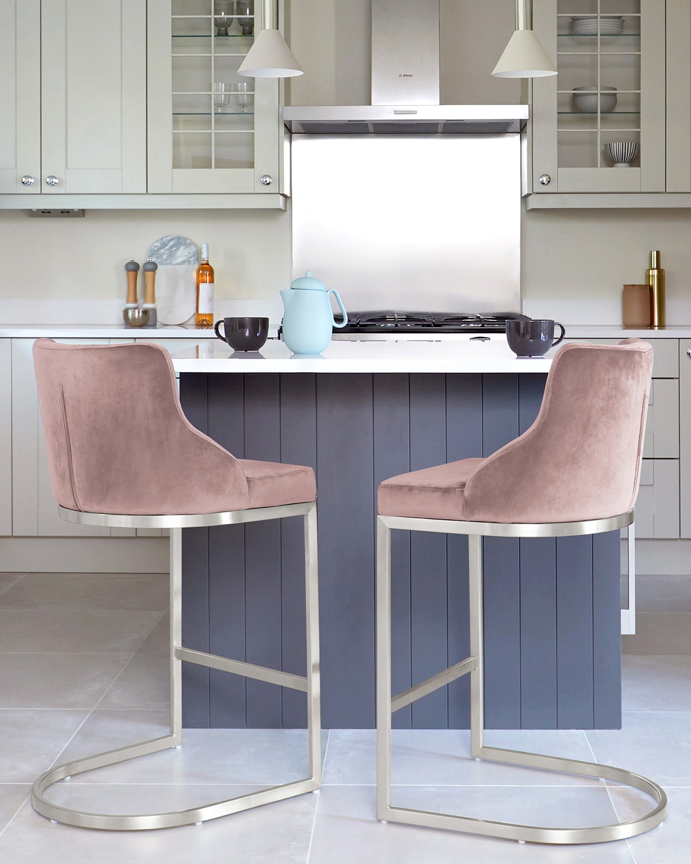 Modern kitchen with two plush velvet bar chairs in a soft pink colour, featuring a curved backrest and a sleek metallic silver base that includes a circular footrest.