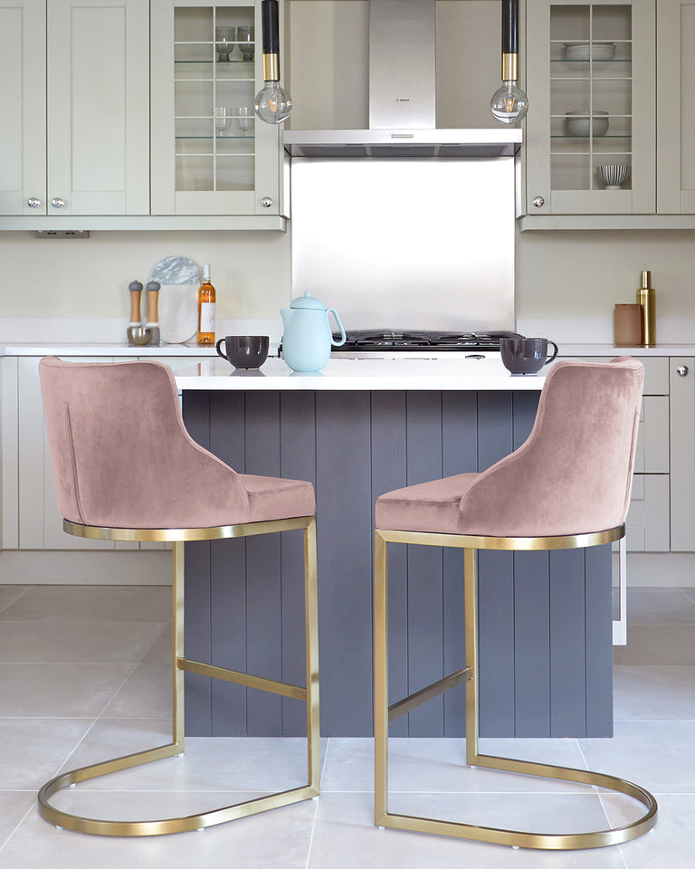 Two modern velvet bar stools with a rounded back design and gold-finished metal legs, set against a kitchen island.