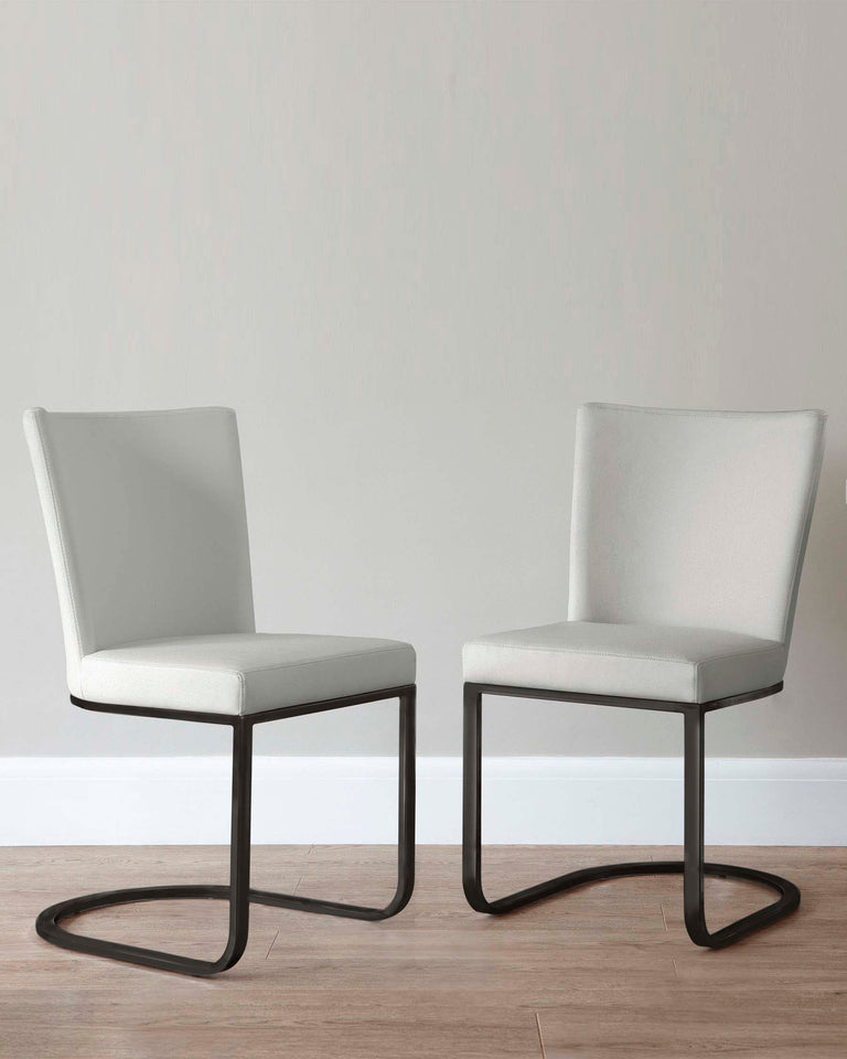 Two modern minimalist dining chairs with cream-colored fabric upholstery and sleek, black metal frame bases in a cantilever design, set against a neutral wall on a wooden floor.