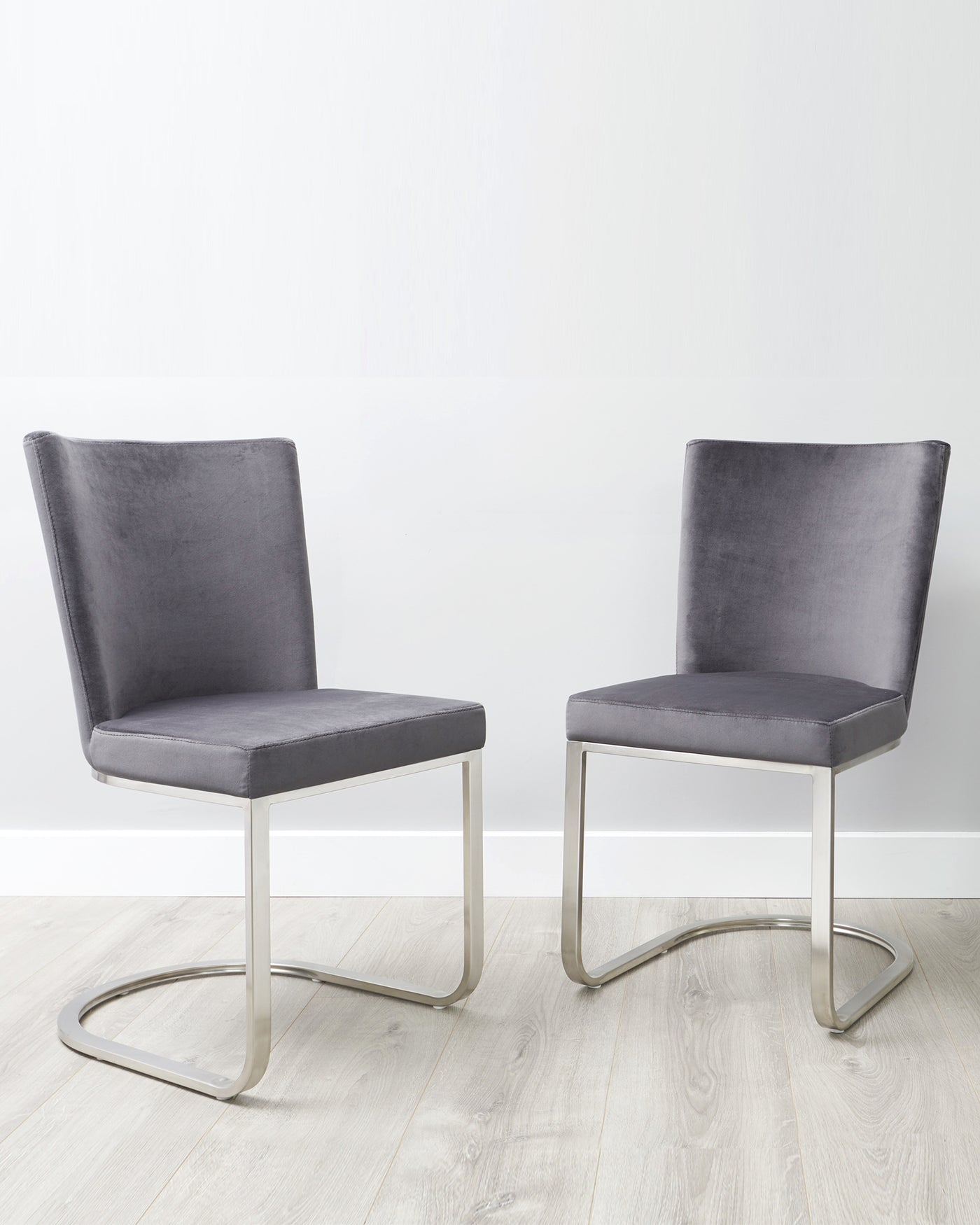 Two contemporary grey upholstered dining chairs with sleek silver metal cantilever bases.