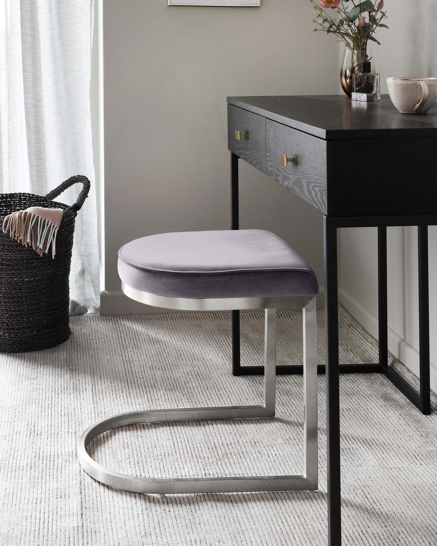 A modern black wooden writing desk with gold-tone drawer pulls paired with a contemporary oval-shaped grey upholstered stool featuring a unique metallic base.