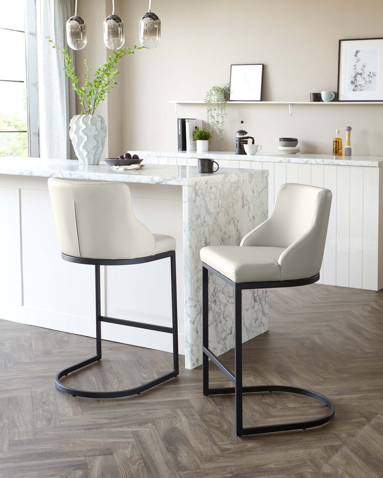 Two contemporary bar stools with sleek beige upholstery and slim black metal legs positioned at a modern kitchen island with marble countertop.