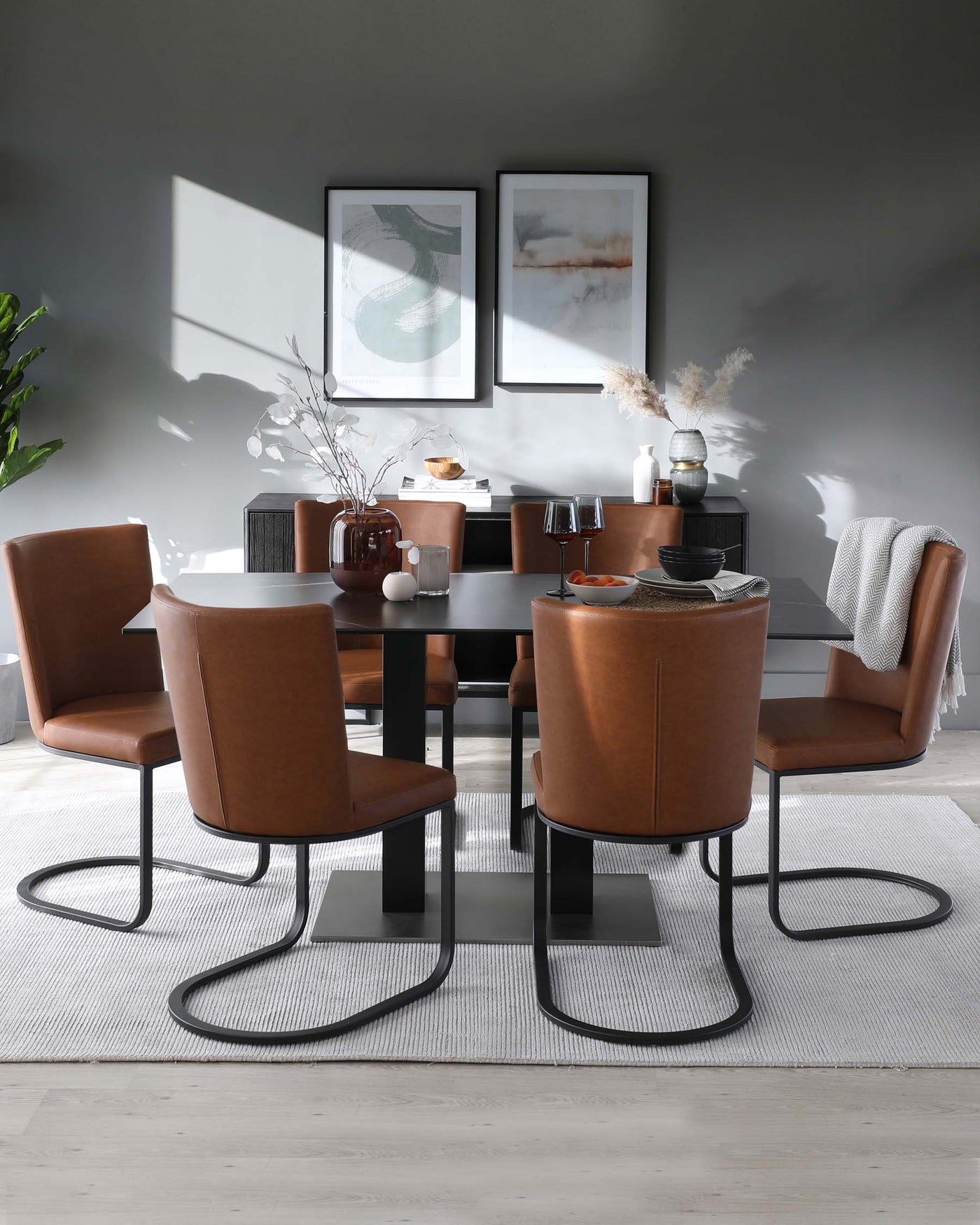 A modern dining room set with a sleek black rectangular table and four matching armchairs with curved cantilevered bases. The chairs are upholstered in a smooth caramel brown leatherette with generous cushioning. The set rests on a textured light grey area rug, accentuating the contemporary design.
