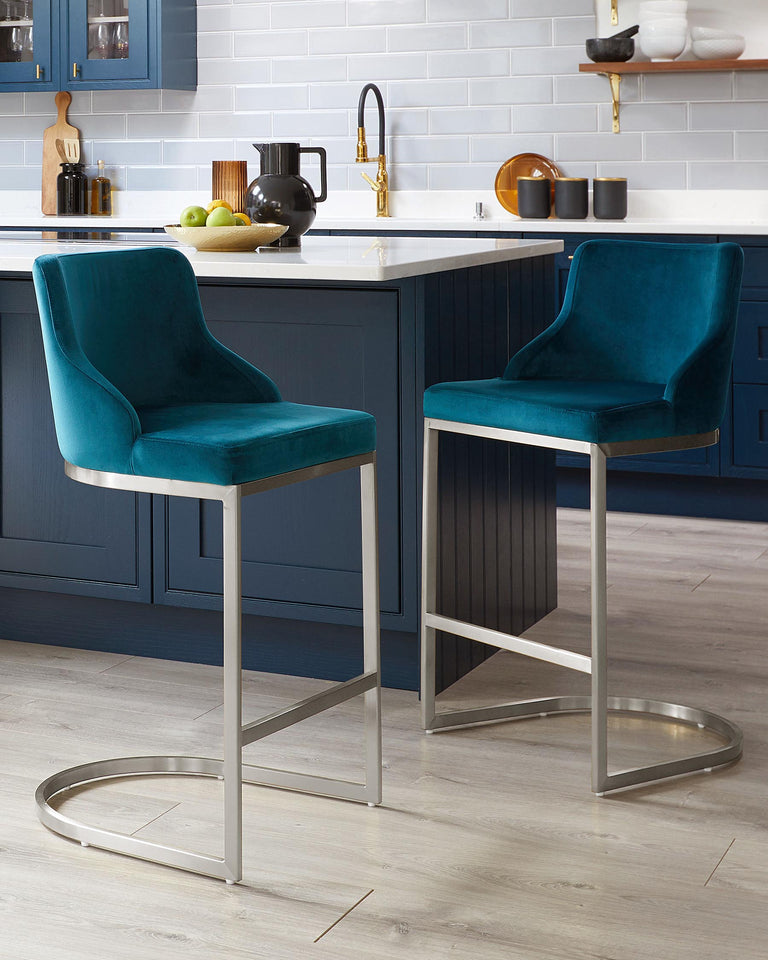 Two teal blue upholstered bar stools with low backs and metallic silver bases, positioned at a kitchen island with white countertop and navy blue cabinetry.