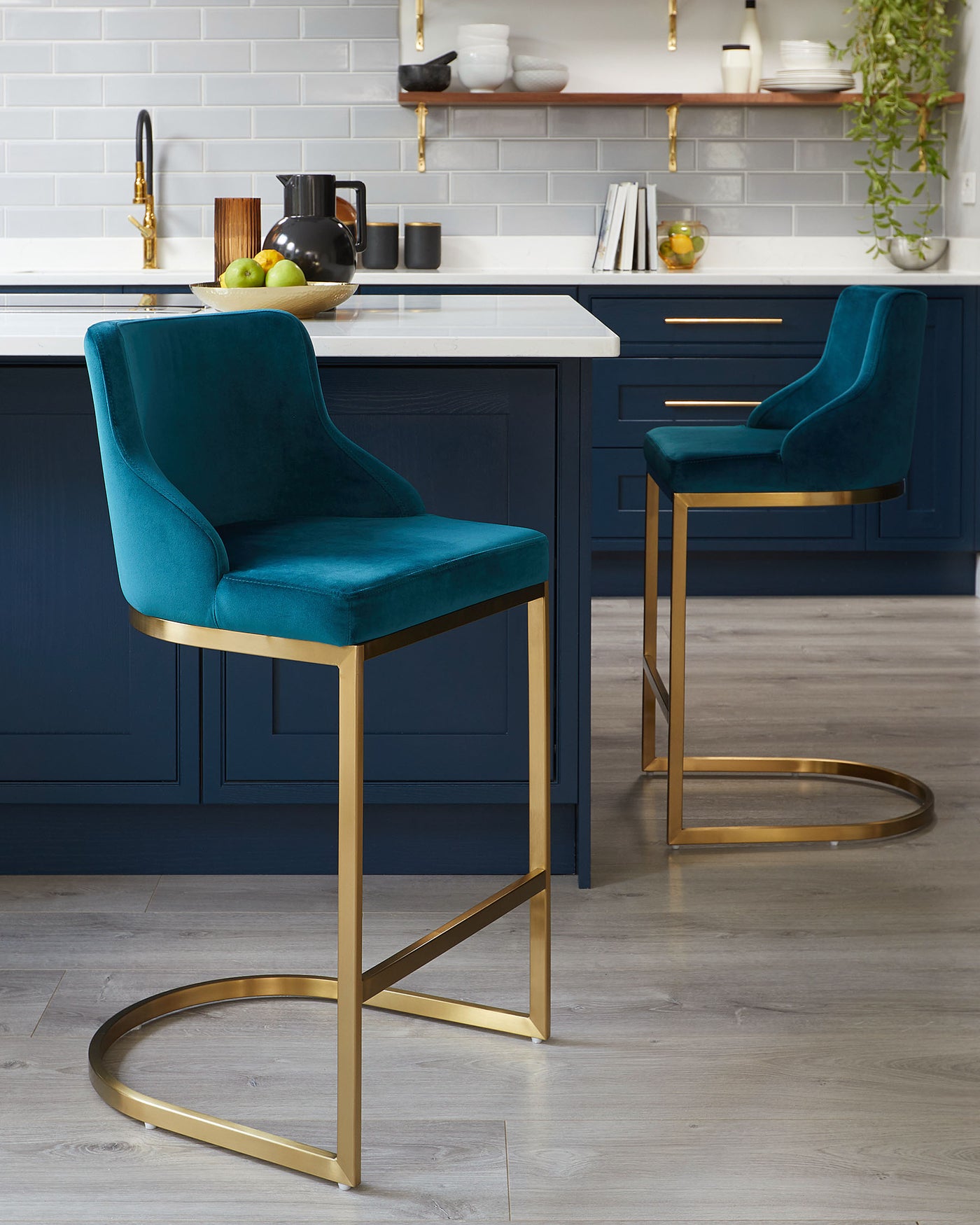 Two modern velvet upholstered bar stools with luxurious teal fabric and sleek gold metal frames, featuring a high back and integrated footrest for comfort and elegance, set against a contemporary kitchen island.