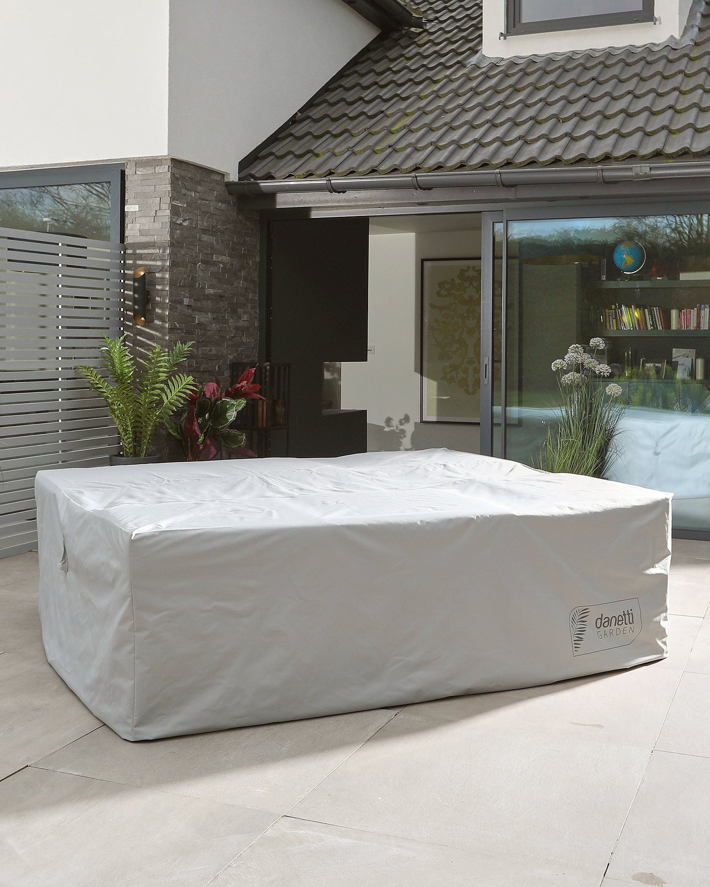 Outdoor furniture piece protected under a white waterproof cover, featuring a logo on the side, situated on a patio area near an open sliding door.