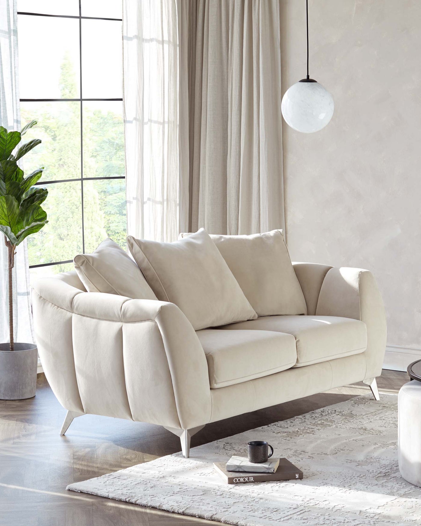 Modern two-seater sofa with a sleek design, featuring a smooth cream fabric upholstery and curved armrests. Stands on slender, angled metallic legs. A cosy, contemporary piece suitable for a chic interior decor.