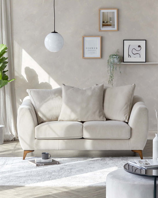 Modern elegant three-seater sofa with plush cushions and a curved silhouette, upholstered in a light cream fabric with tapered wooden legs. Paired with a round coffee table featuring a combination of a reflective black top and a muted grey bottom. Set upon a textured white area rug.