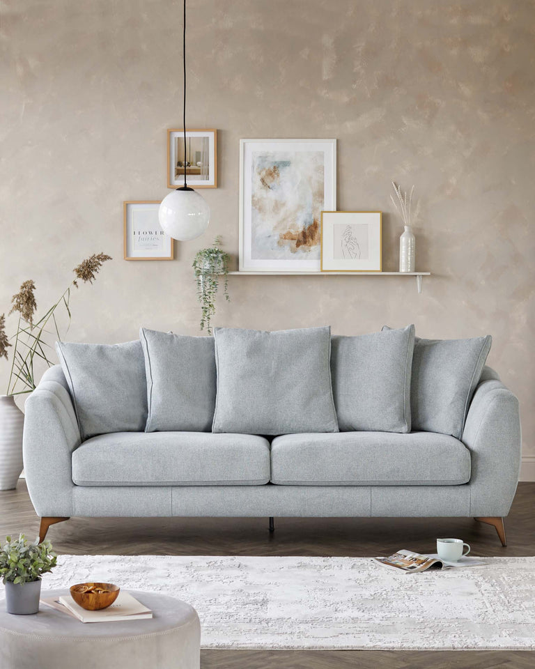 Elegant mid-century modern light grey fabric sofa with clean lines, featuring plush back cushions and a tufted bench seat. The sofa rests on tapered wooden legs with discreet black metal tips, complementing the minimalist aesthetic. A round, velvet-upholstered ottoman in a muted grey tone serves as a central coffee table, providing a soft contrast to the distressed white patterned area rug beneath.