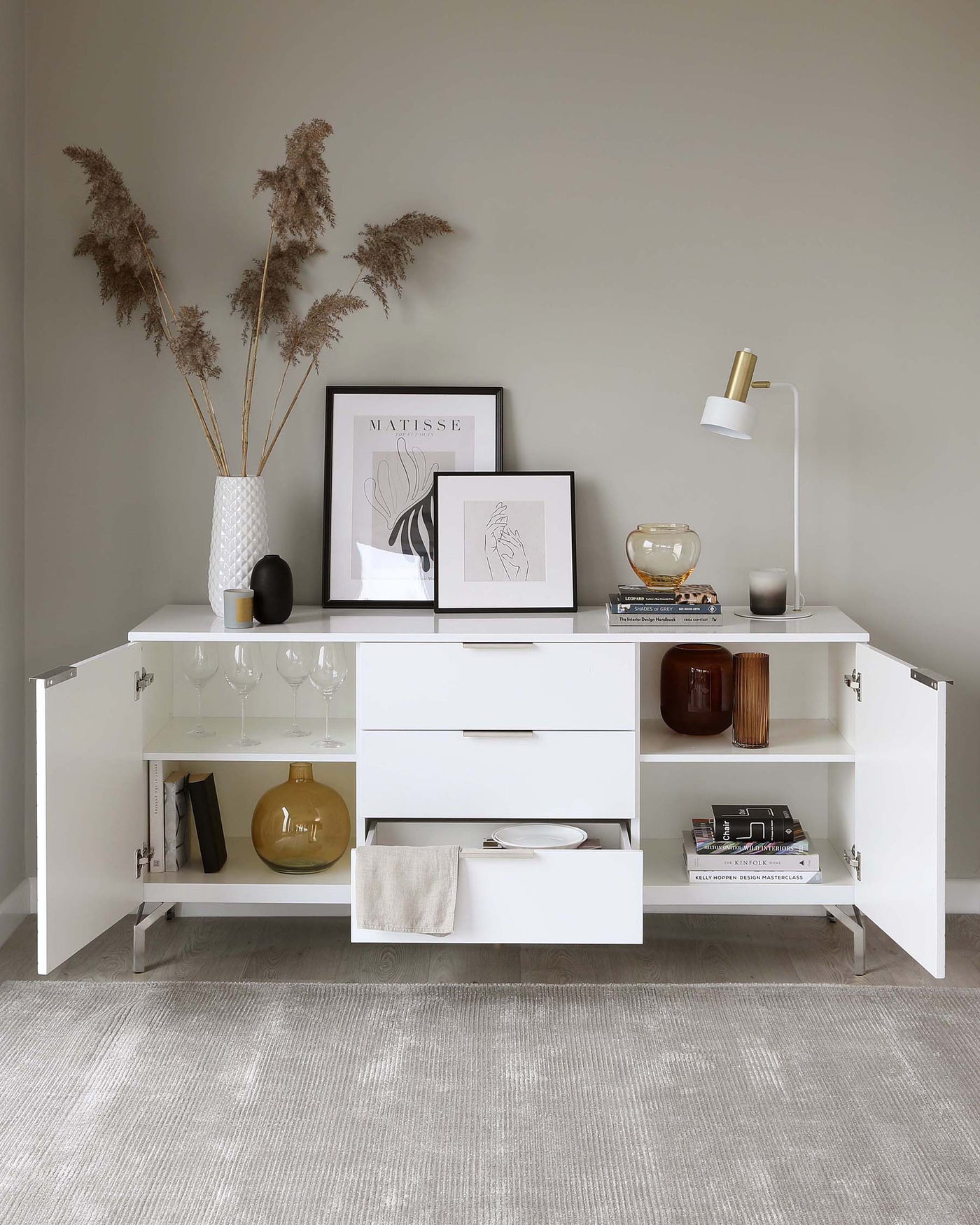 Modern white sideboard with multiple storage compartments, including shelves, drawers, and hinged cabinets, accentuated with minimalist metallic handles, on a light grey textured flooring.