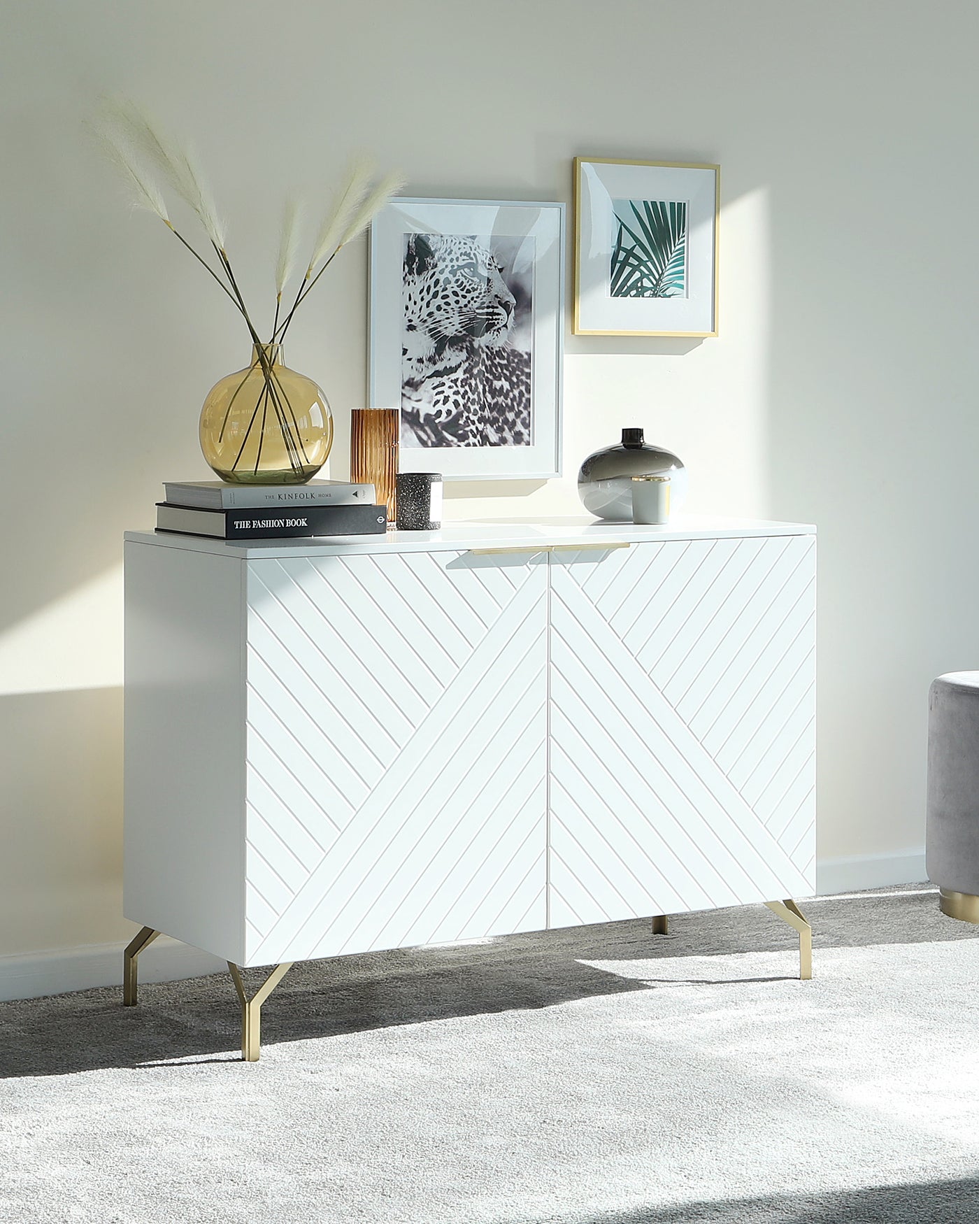 Modern white sideboard with geometric-patterned front panels and gold-coloured metal legs, positioned against a light-coloured wall on a grey area rug.