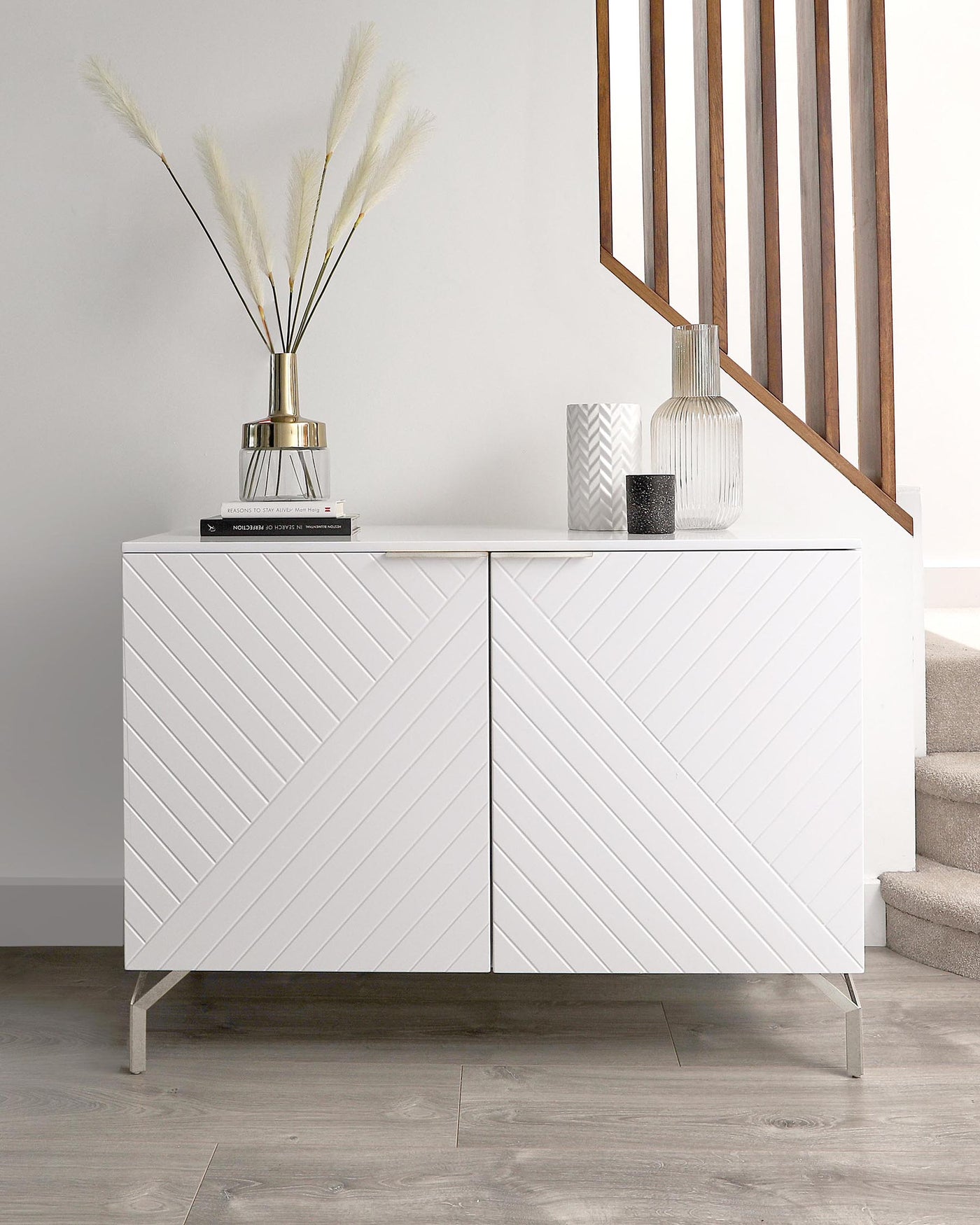 A modern white sideboard with a geometric chevron pattern on its doors and sleek metal legs.