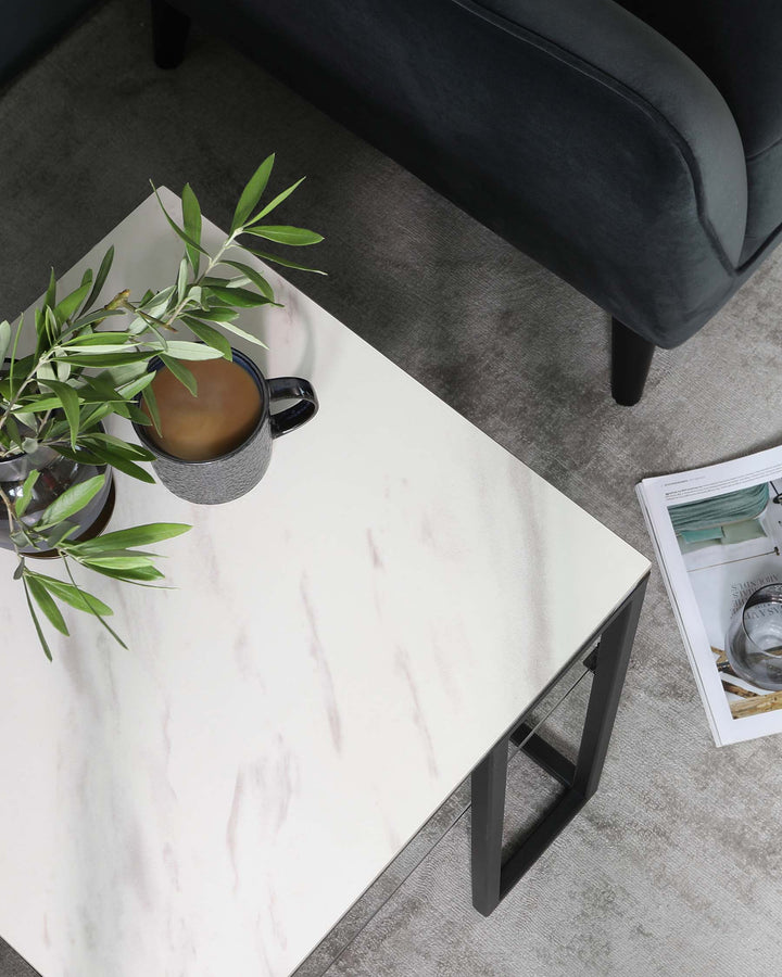 A contemporary marble-top coffee table with a minimalist black metal frame, positioned next to a dark upholstered sofa with visible sleek legs, all set on a textured grey area rug.